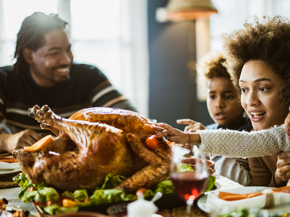 A joyful family with a young child reaches for a roasted turkey on a festive table during a holiday meal, expressing excitement and happiness.