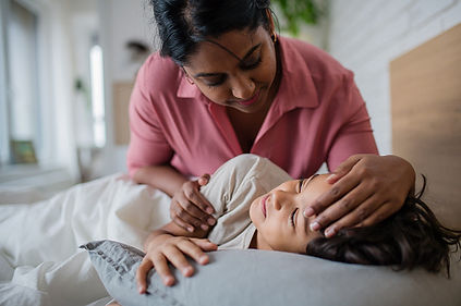 A woman in a pink shirt tenderly strokes the forehead of a young boy as he rests on a pillow, depicting a caring and comforting moment.

.