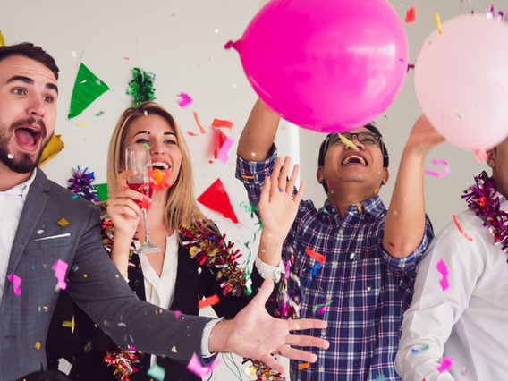 Four joyful people celebrating with balloons, confetti, and drinks in a festive atmosphere. they are laughing and reaching towards colorful balloons.