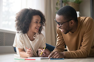 A man and a young child smiling at each other while drawing together at a table. they appear happy and engaged in their activity, surrounded by colored pencils and paper.