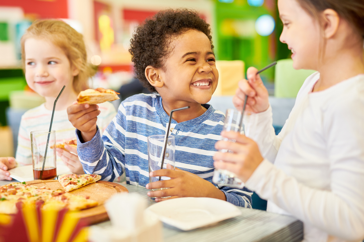 Colorful portrait of multi-ethnic group of children eating pizza enjoying awesome party in cafe, focus on African-American boy laughing happily