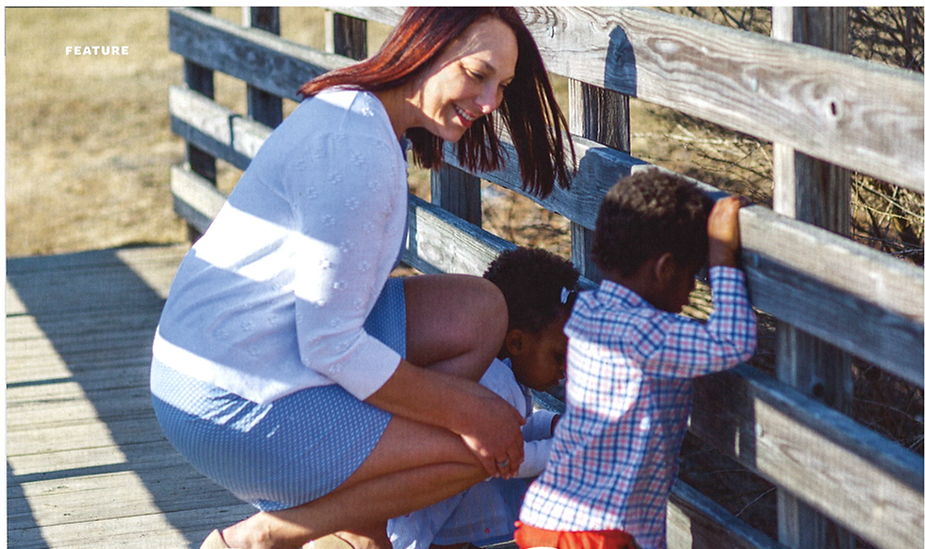 A woman crouching in a comforting embrace with two children at a wooden fence, all enjoying a sunny day outdoors.