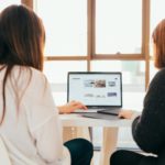 Two women look at a laptop screen.