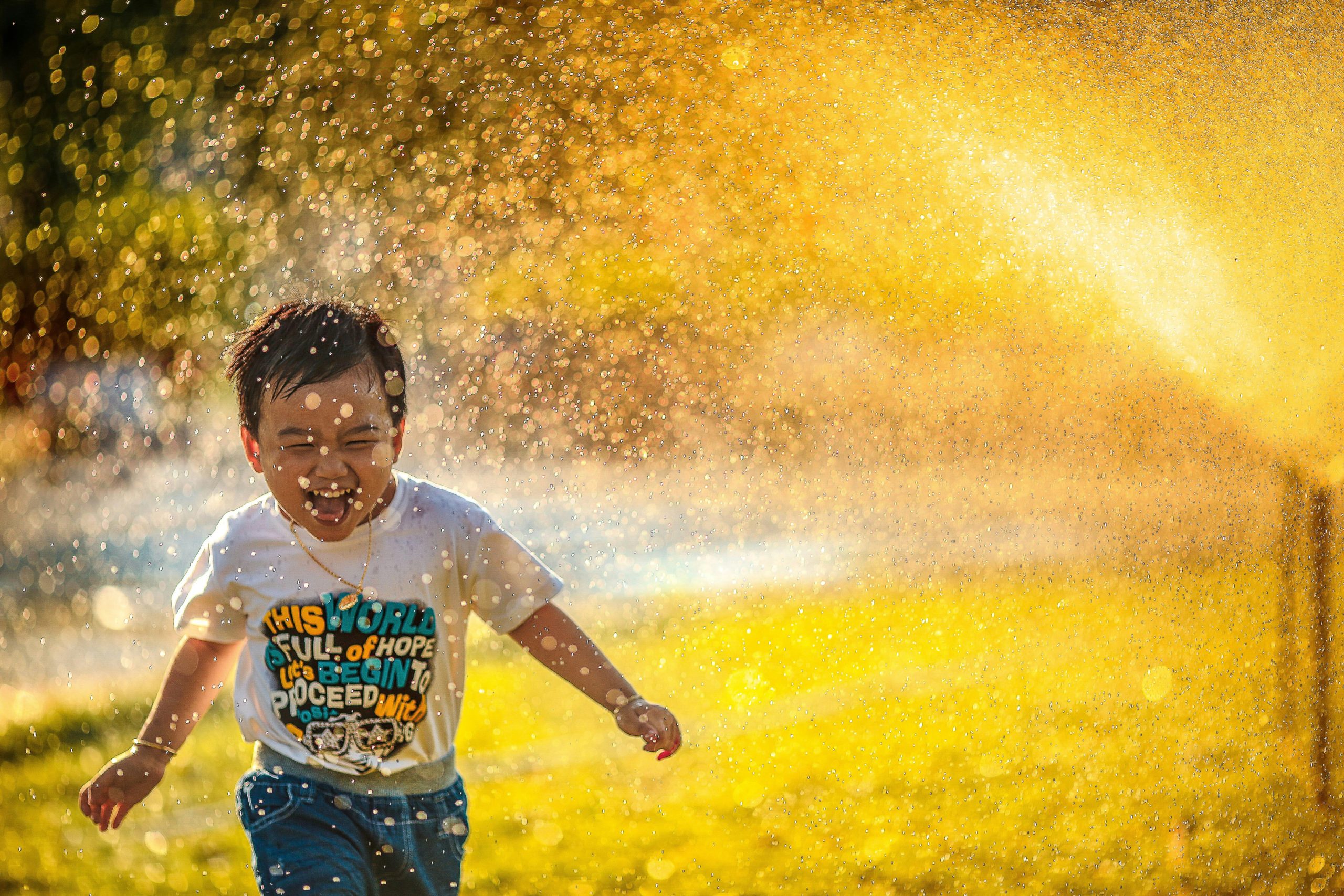 Foster child runs through sprinklers in the summer sunshine.