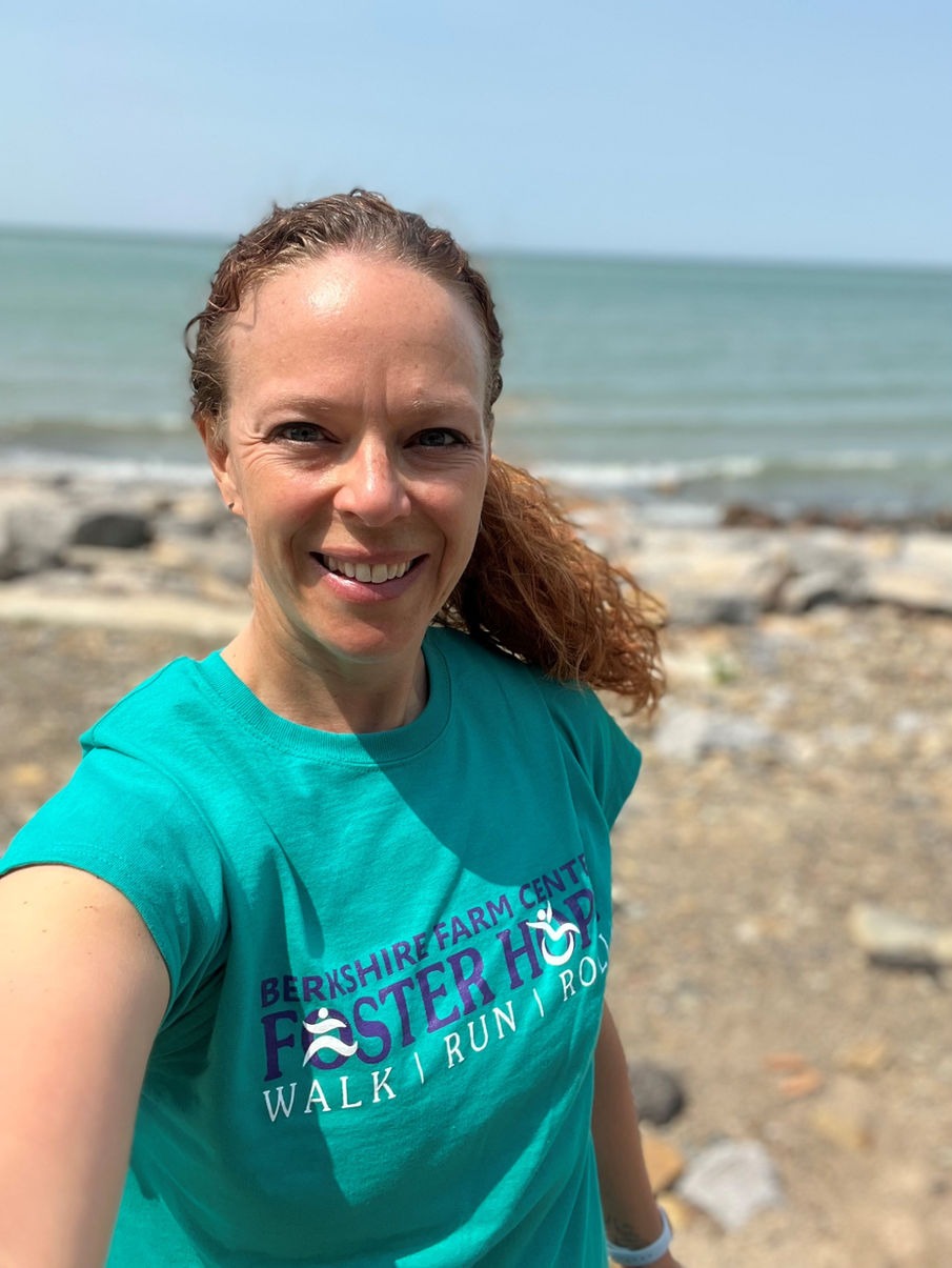 A woman with curly hair smiling at the camera in front of a seaside backdrop, wearing a teal 