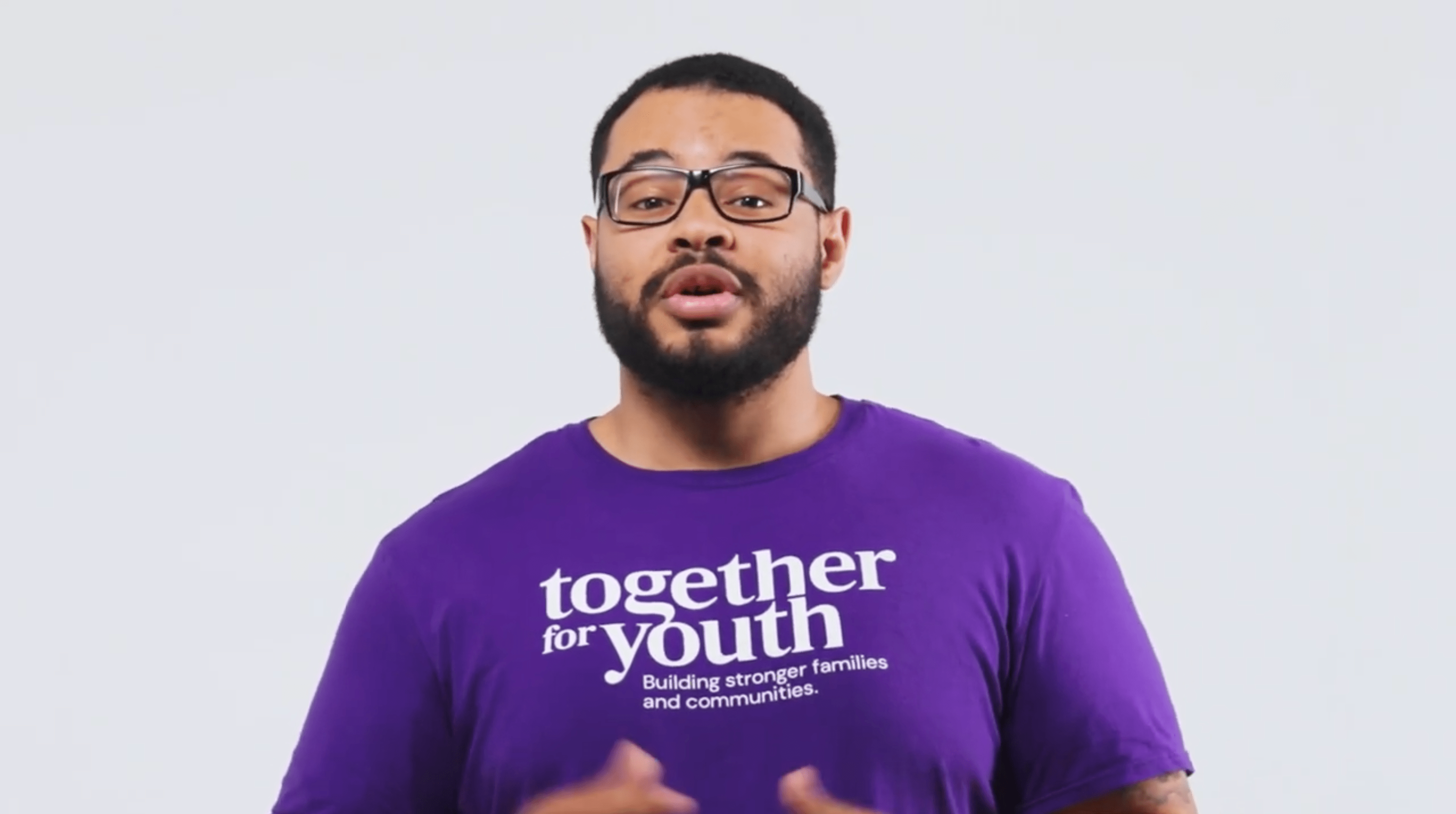 Troy with short hair, beard, and glasses is wearing a purple T-shirt that reads 