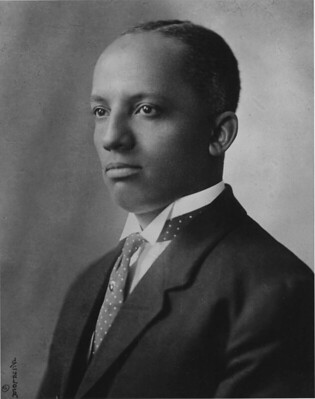 Portrait of a man in a suit with a polka dot tie, looking to the side. The image is black and white, with a neutral background. His expression is calm and composed.