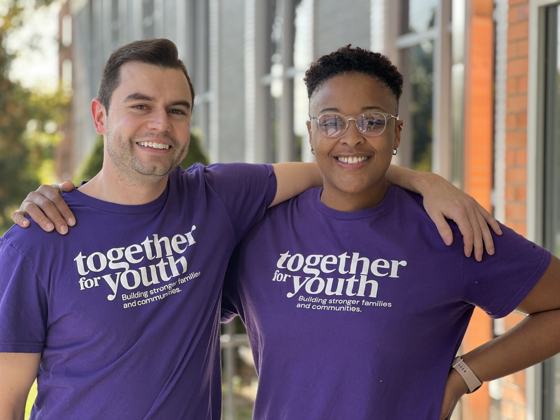 Two people smiling and standing side by side, each wearing a purple 